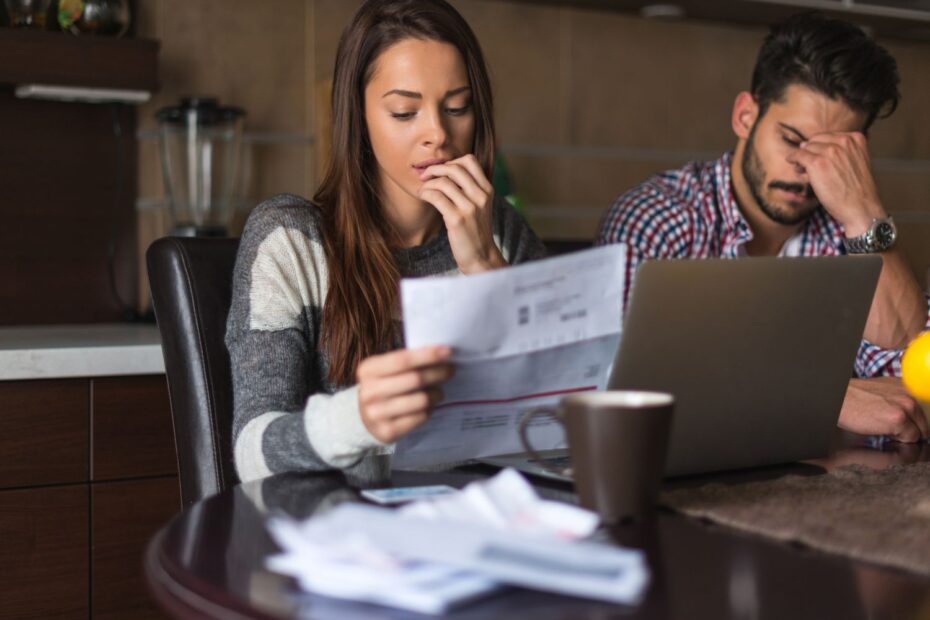 a woman holding an electrical bill and looking worried while a man beside her holds his head in his hands