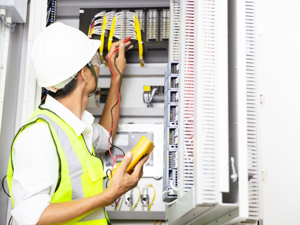 a man in a hard hat and vest inspecting an electrical panel
